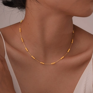 Close-up of minimalist gold bead chain necklace worn on neck for a layered look