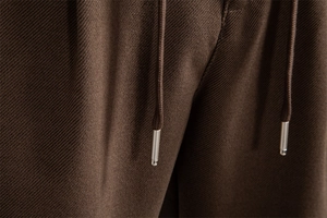 Macro detail of dark brown twill fabric texture and metal tipped drawstring on men's trousers