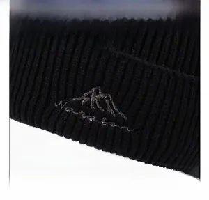 Detail of black rib-knit beanie showing fine embroidery of silver mountain peaks