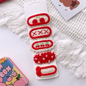 Detailed view of five handcrafted knit hair clips with cherry and bow patterns on card