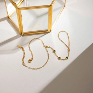 Gros plan d'un bracelet en chaîne dorée avec trois pierres précieuses vert émeraude