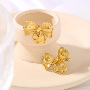 Elegant gold bow earrings with textured finish on a ceramic jewelry display stand