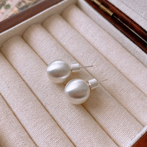 Macro view of silver brushed sphere stud earrings resting on beige velvet jewelry tray