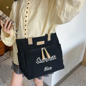 Detail of black canvas tote bag with beige straps and white summer embroidery text
