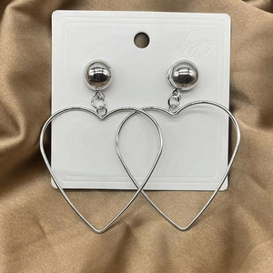 Detailed view of oversized hollow heart earrings on white card with golden satin background