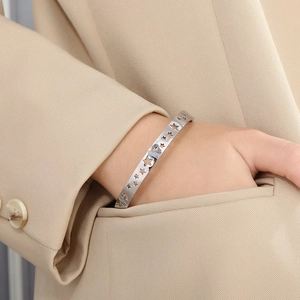 Close-up of a silver hollow star bangle on a model's wrist against a beige suit pocket