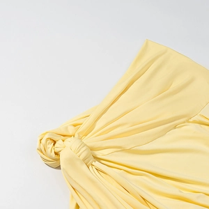 Detailed close-up of light yellow knit dress featuring waist knot and soft pleats