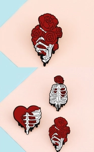 Three enamel pins featuring skulls and red roses on a pastel pink and blue background