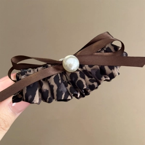 Leopard print bow hair clip with brown satin and white pearl accent on warm background