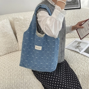 Sac fourre-tout en jean bleu à motifs nœuds porté par un mannequin sur un canapé