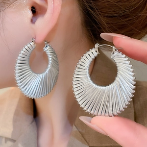 Détail des boucles d'oreilles créoles géométriques argentées portées sur l'oreille