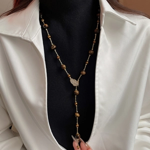 Detail of tiger eye bead necklace with zircon leaf pendant on a model's white shirt