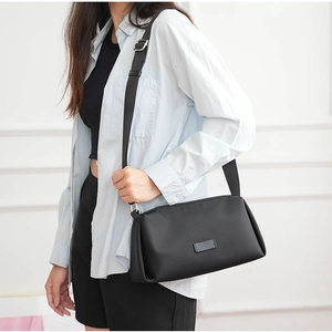 Vista lateral de bolso bandolera de nailon negro con correa ancha en una modelo