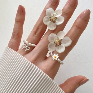 Elegant pearl bead rings featuring silver bow charm and daisy flower on model's hand