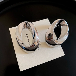 Detail of twisted oval silver metal earrings with a polished mirror finish on black tray
