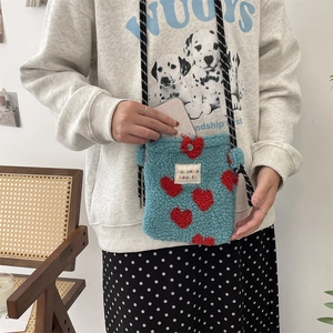 Detail of blue plush crossbody bag with red heart clasp and striped braided rope strap