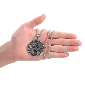 Détail du pendentif argenté Saint Michel porté par une main sur fond blanc