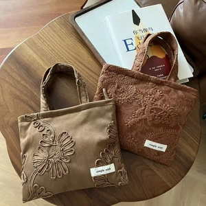 Macro shot of embroidered suede tote bags with floral patterns and brand labels