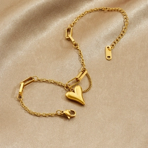 Gold heart pendant bracelet with mixed chain links on elegant silk fabric background
