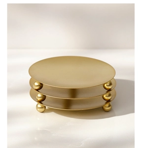Detail of three matte gold round metal trays with ball feet on a white marble surface