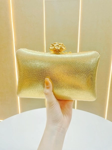 Detail of a golden glitter evening clutch featuring a delicate metal flower-shaped clasp