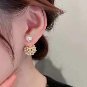 Detail showing gold-plated mesh hollow sphere and white pearl earrings on model ear
