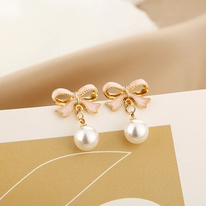 Macro detail of pink ribbon bow earrings with round white pearl drop and gold metallic trim