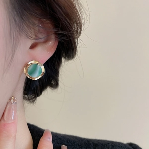 Detail of a vintage pearl earring with green gemstone inlay on model ear