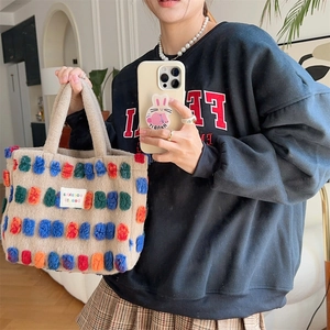 Plush beige bucket bag with colorful pom-pom details and a soft lamb wool texture