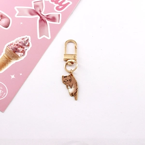 Detail of cute light brown kitten keychain with golden D-ring clasp on pink card