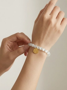 Close-up of white cat eye bead bracelet with a golden Fu character round charm