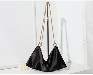 Detail of black satin tote bag with elegant gold chain strap and soft triangular texture