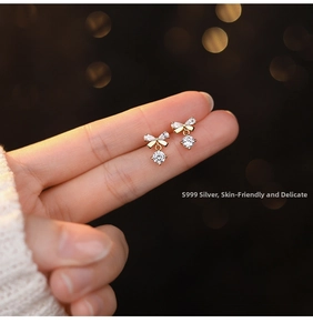 Detailed close-up of a delicate golden bow stud earring with a sparkling round zircon stone
