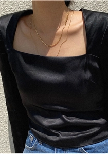 Detail of a minimalist gold cross necklace styled with a black satin square-neck top