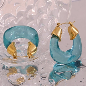 Macro shot of green acrylic U-shaped earrings on a clear glass surface with water drops