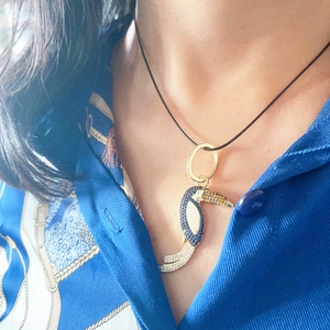Close-up of a golden toucan bird pendant with colorful gemstones on a black cord