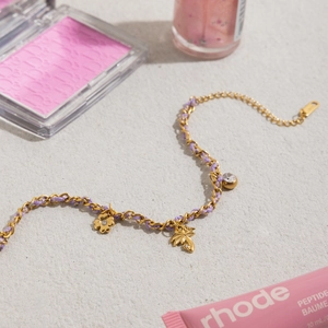 Detail of gold chain and purple woven cord bracelet with floral and palm tree charms