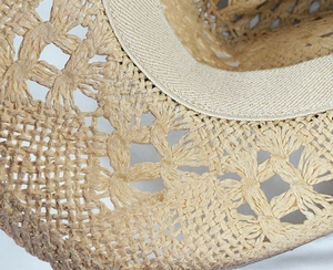 Vista macro della trama in paglia intrecciata e motivi traforati su un cappello cowboy