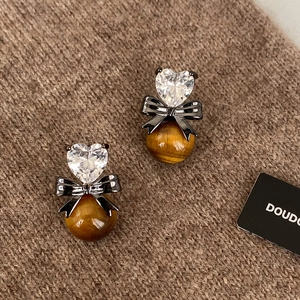 Macro detail of heart zircon earrings with black bow and tiger eye beads on knit background
