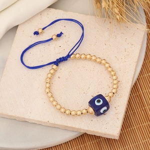 Adjustable evil eye braided bracelet with gold beads on a natural stone background