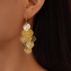 Close-up of gold hollow geometric tassel earrings worn by a model with long hair