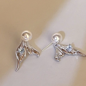 Detailed macro of fishtail earrings with pearls and a small blue heart gemstone