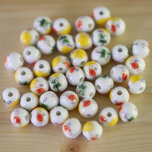 Macro detail of white ceramic beads with colorful hand-painted floral patterns on wood