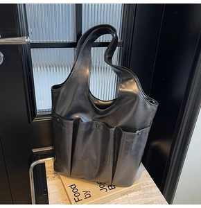 Detail of black leather tote bag with functional vertical pockets on a minimalist marble background