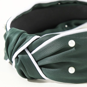 Detail of dark green knot headband with pearl embellishments and white piping trim
