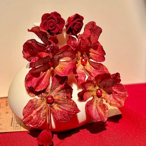 Detailed view of red fabric rose earrings with rhinestones on a white ceramic display