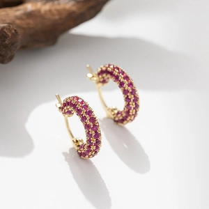 Detail of gold hoop earrings with pavé set pink zircon stones on a wooden stand