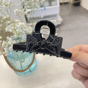 Detail of a glossy black polka dot bow hair claw clip held against a lifestyle background