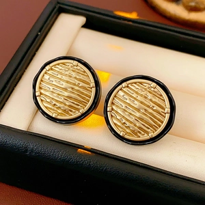 Detailed macro of gold textured stud earrings with black enamel trim in a gift box