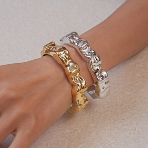 Detail of irregular lava texture gold and silver open bracelets on female model wrist